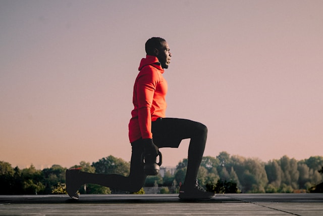 Een man doet buiten een lunge met een kettlebell bij zonsopkomst.